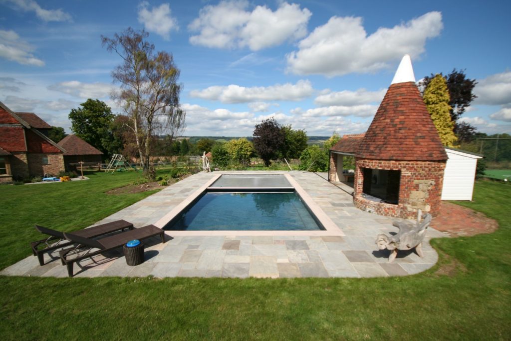 Oast House Pool in Kent in charcoal mosaic tiles, sandstone paving and a grey automatic safety cover.