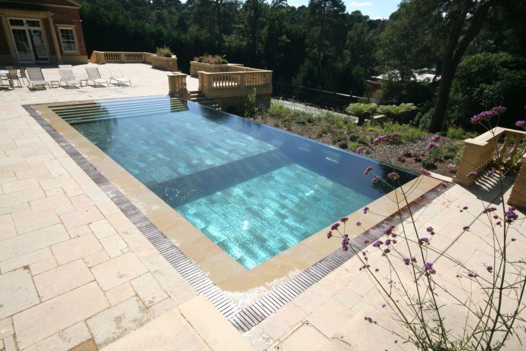 Infinity edge pool with wall windows and automatic slatted cover, full width steps and large format tiles