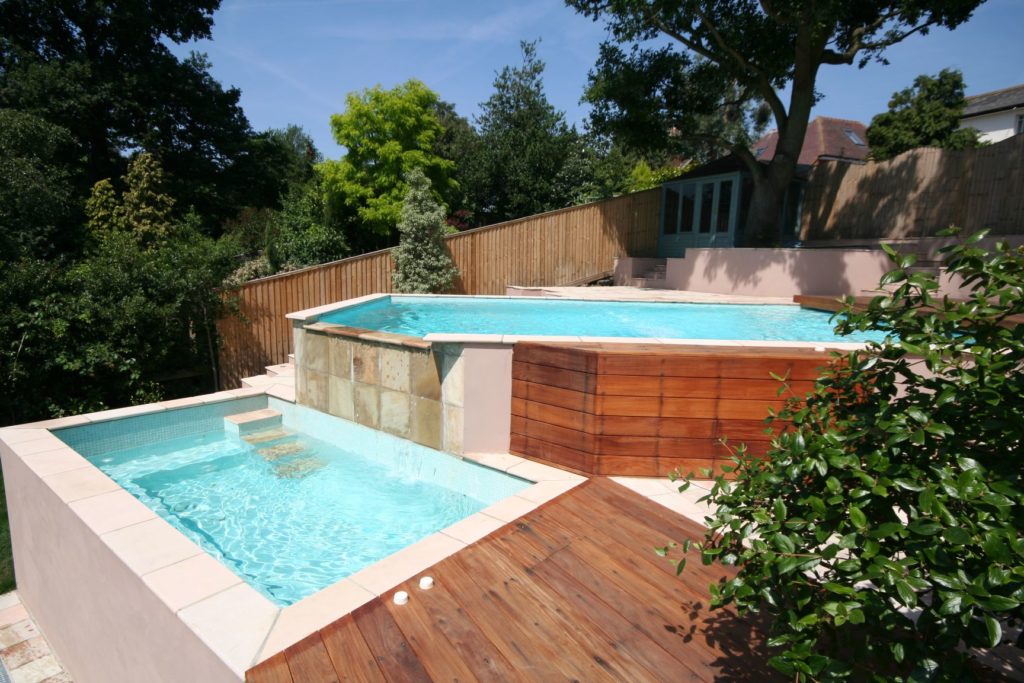 Built into a hillside with no digger access, this pool was hand dug and all spoil removed by wheelbarrow. The pool features a slatted cover with a waterfall over the wall into the spa below.